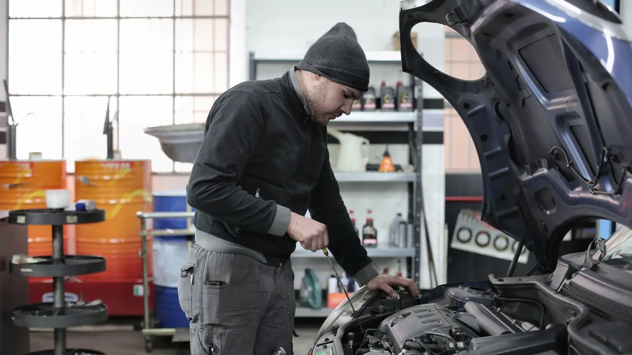 Kışlık bereli usta serviste kaputu açık aracın motor yağını kontrol ediyor